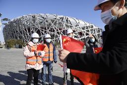 <p>　北京冬季五輪の開閉会式が行われる国家体育場前で、記念撮影用の中国国旗を持つマスク姿の人たち＝２月、北京</p>