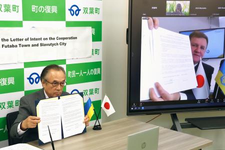 <p>　原発事故に関する知見の共有に向けた連携協定の締結式をオンラインで開き、署名した福島県双葉町の伊沢史朗町長（左）とスラブチチ市のフォミチェフ市長＝２６日午後、双葉町役場</p>