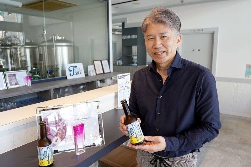 「ヒノキ森の賢者」の瓶ビールを持つスリラービーチブルワリーの笠倉さん=勝浦市