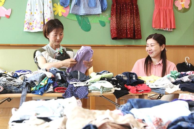 「子ども服交換会」で服を選ぶ親子と「ＡｗａｄｅＫｏｓｏｄａｔｅ」の笹生代表（右）＝鋸南町