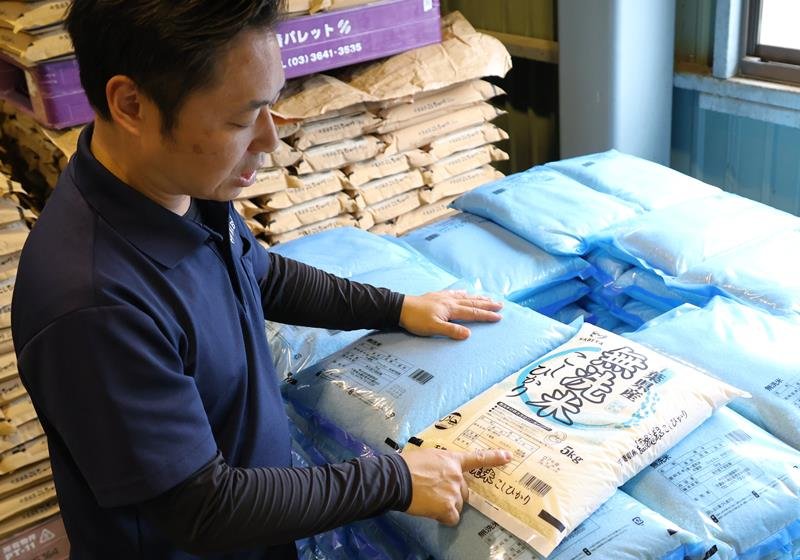 イラストが描かれていないシンプルな無洗米用のコメ袋を紹介する斎藤さん。手前は通常デザインのコメ袋=6月、大網白里市