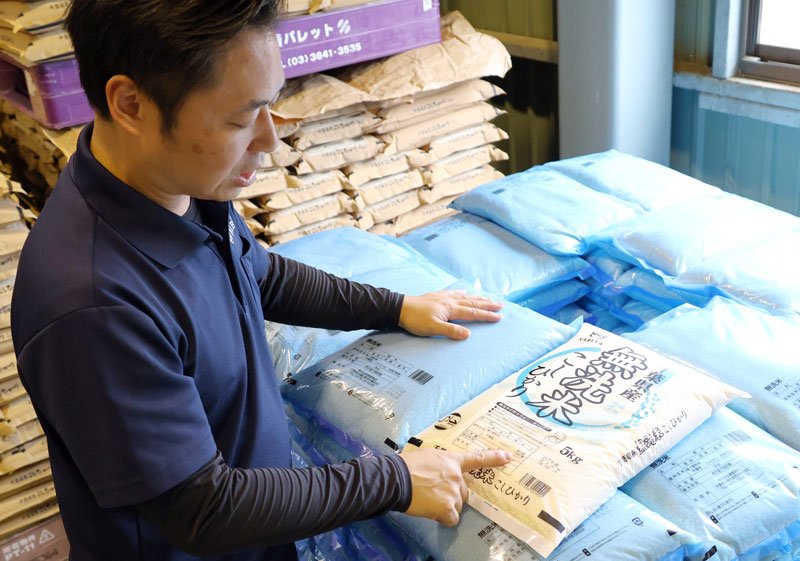 イラストが描かれていないシンプルな無洗米用のコメ袋を紹介する斎藤さん。手前は通常デザインのコメ袋=6月、大網白里市