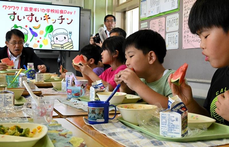 五十嵐市長(左)とスイカ給食を楽しむ富里第一小学校の児童=17日、富里市