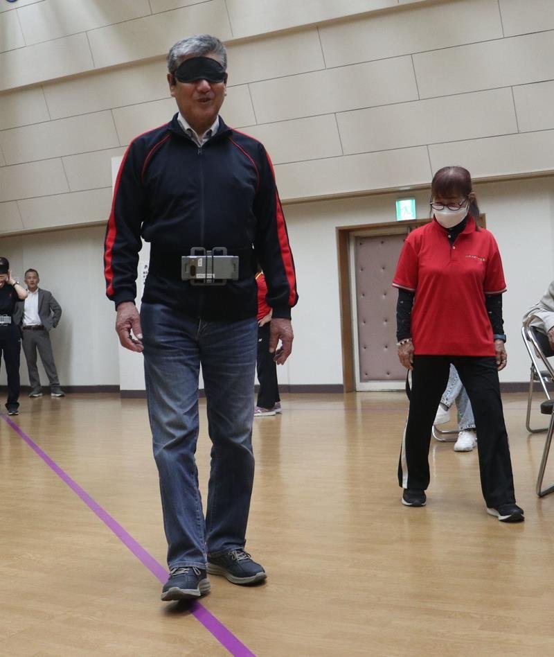ヘッドフォンへの音声シグナルを頼りに紫色の線に沿って一人で歩く視覚障害者の男性=茂原市