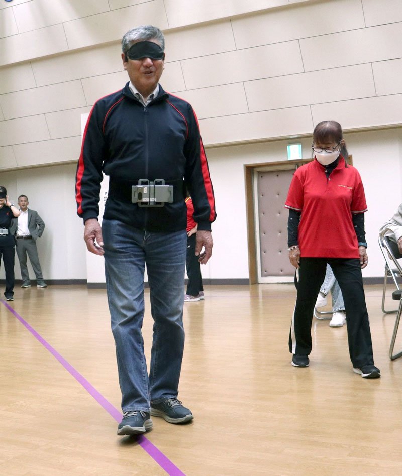 ヘッドフォンへの音声シグナルを頼りに紫色の線に沿って一人で歩く視覚障害者の男性＝茂原市