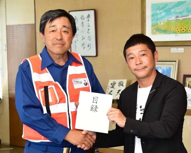 ９月に行われた被災地訪問で、金丸市長（左）に目録を手渡す前澤さん（９月３０日、同市提供）
