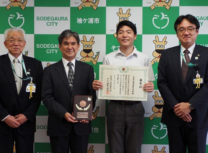 表彰状を伝達されて笑顔を見せる中村さんと盾を手にする佐藤校長＝袖ケ浦市役所
