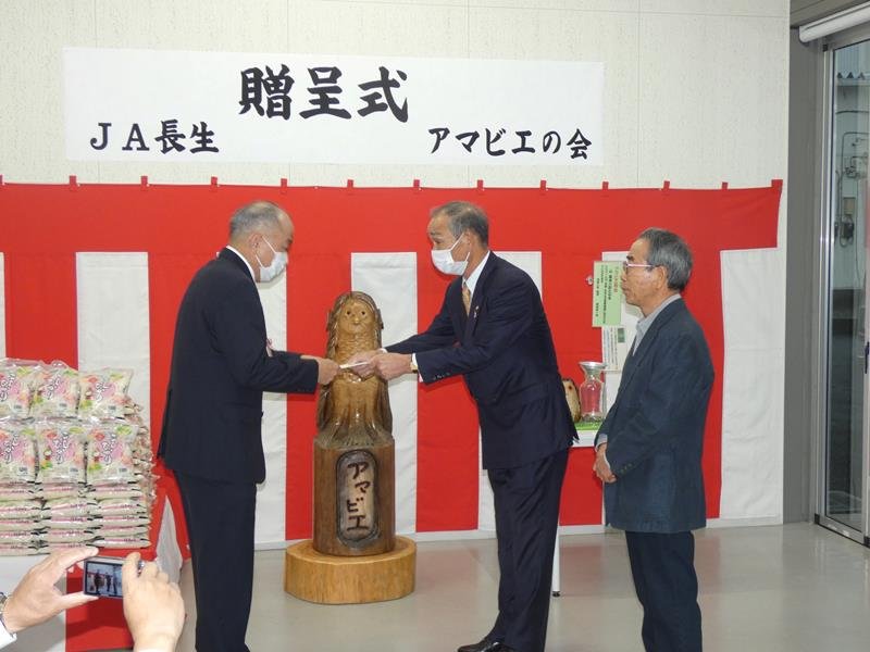アマビエ募金と米の目録を長生病院の牧野事務部長（左）に手渡す河野組合長（中）と像を制作した木村廣志さん（右）＝茂原市のながいき市場

