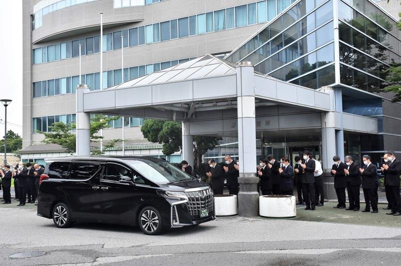 土屋市長のひつぎを乗せた車に手を合わせる勝浦市職員ら＝１６日午後、同市役所
