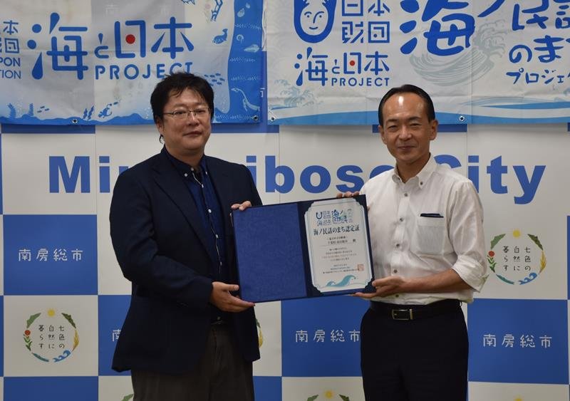 認定証を掲げる石井市長（右）と事業プロデューサーの柴田氏＝南房総市役所
