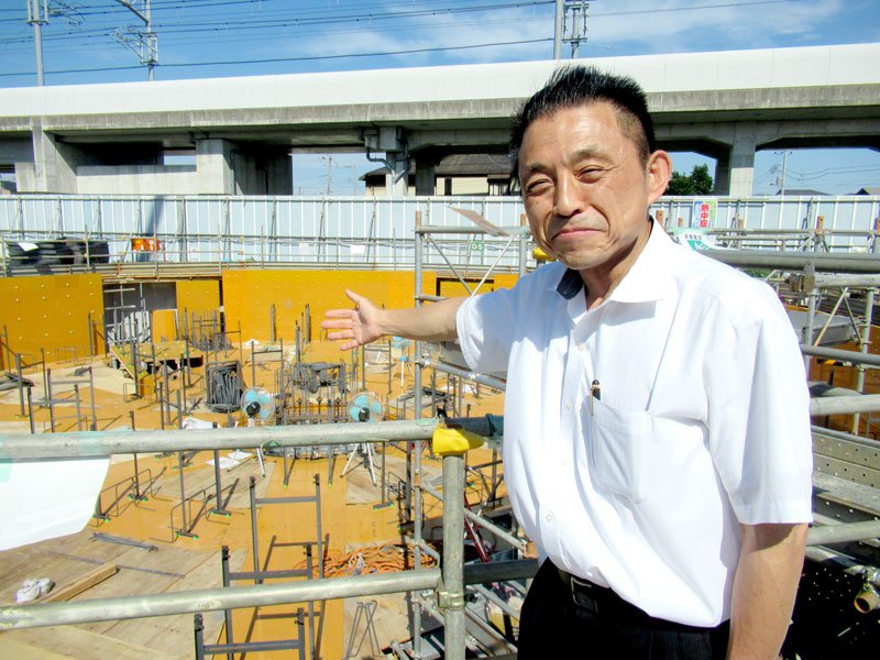 基礎部分が建設中の木造高層ビルと西峰社長。ビルの名前を「ｋｉｎｏｂｉｒｕ」とつけた＝鎌ケ谷市