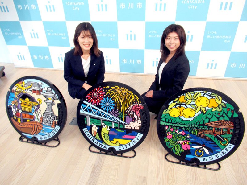 新デザインの３種類のふたと、制作を担った石井麻沙美さん（右）、今井英里奈さん（左）＝市川市役所
