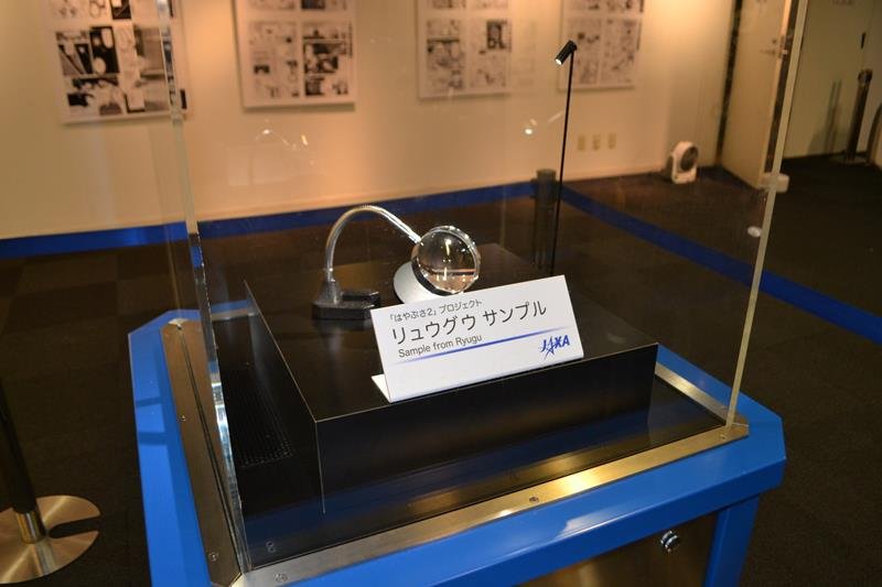 リュウグウのかけらが千葉市科学館で展示されている様子。大きさは数ミリほどで拡大鏡で観察できる＝同市中央区
