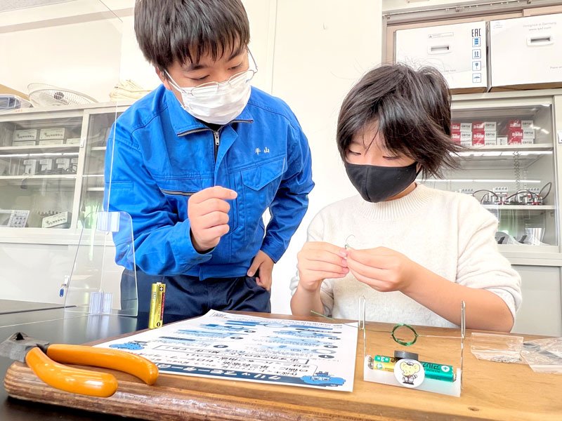高校生（左）にアドバイスを受けながら、モーターの製作に挑戦する小学生＝市原市の姉崎高校