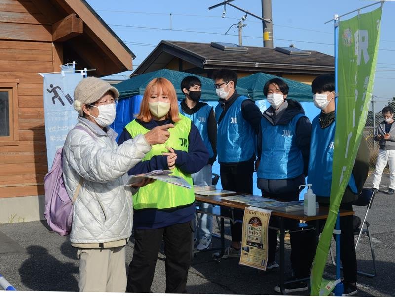ハイキングツアー出発地のＪＲ求名駅で参加者の女性（左）を案内する城西国際大の学生＝東金市
