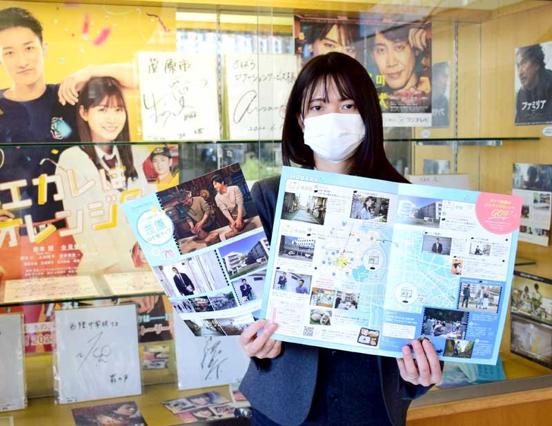 最新のロケ地マップを持つ担当者。茂原市役所には出演者のサインや作品情報を展示するコーナーがある＝同市