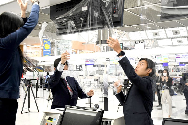 チェックインカウンターから新型コロナ対策の飛沫防止フィルムを取り外すＮＡＡ社員＝８日、成田市