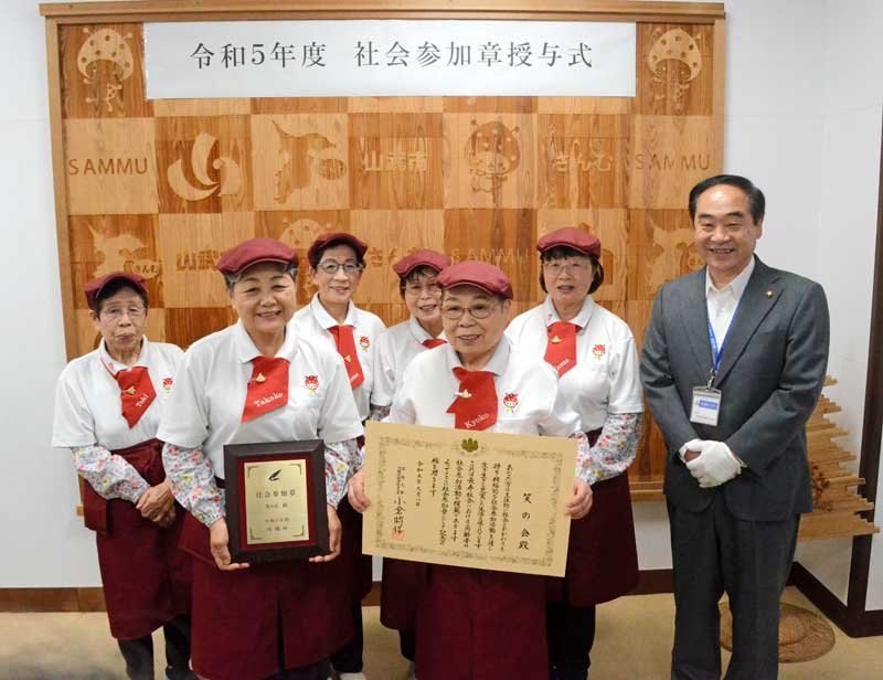 地域密着ピザ店の活動で、賞状や盾を授与され笑顔の「笑の会」メンバー。右は松下市長＝山武市役所