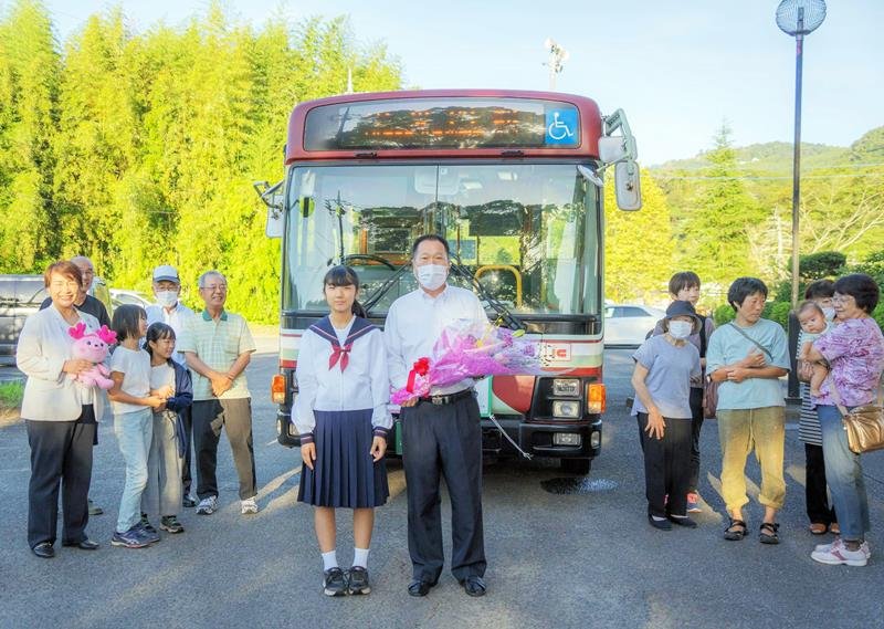 路線バスの復活を喜び出発式に集まった地元住民ら。始発便の運転手に中学生から花束が贈呈された＝君津市（市提供）