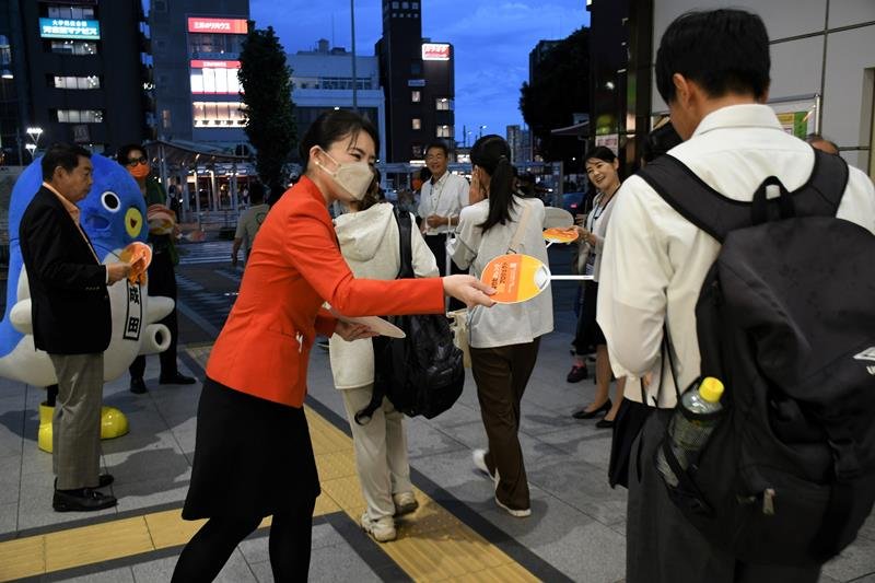 認知症理解への啓発カラーのオレンジ色の制服姿で啓発グッズを手渡す航空スタッフら＝２１日夜、成田市

