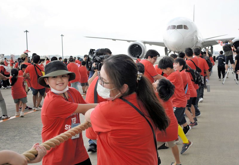 力を合わせ、巨大な航空機を楽しそうに引っ張る親子たち＝１７日、成田空港