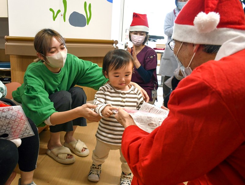 サンタクロースの衣装を着た青墳院長（右）からプレゼントを受け取る子ども＝１８日、成田市の成田赤十字病院