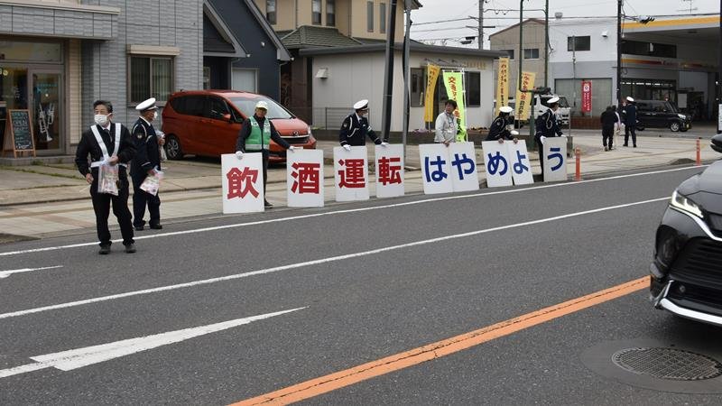 飲酒運転撲滅へプラカードでドライバーに交通ルールの順守を呼びかける関係者。信号待ちの車に駆け寄って啓発物資も配布した＝５日、八街市
