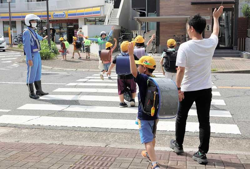 手を上げて横断歩道を渡る下校中の児童＝２４日午後、千葉市稲毛区