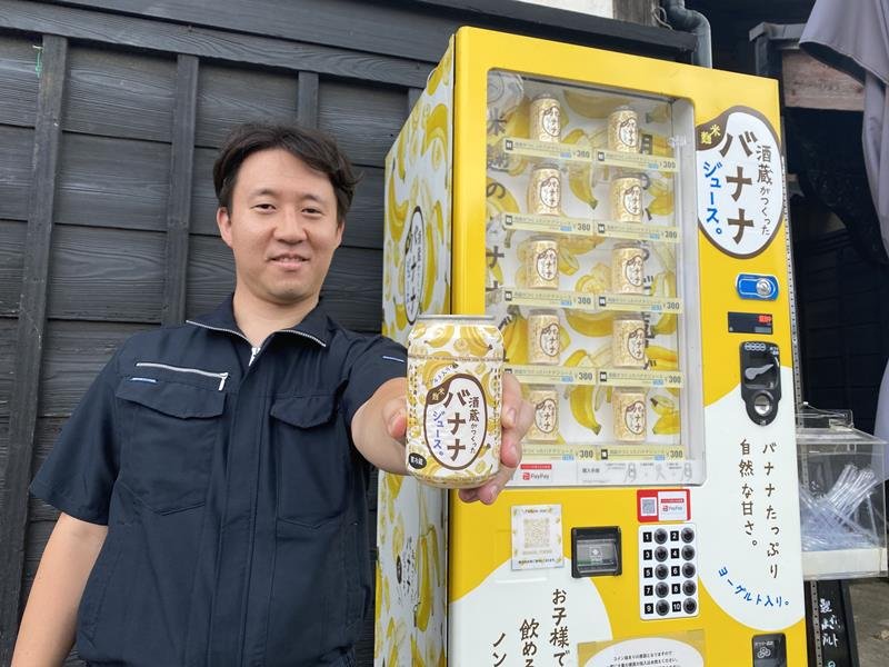 「酒蔵がつくったバナナジュース」を開発した旭鶴の田中源太郎さん。黄色い自販機のデザインにもこだわった＝佐倉市
