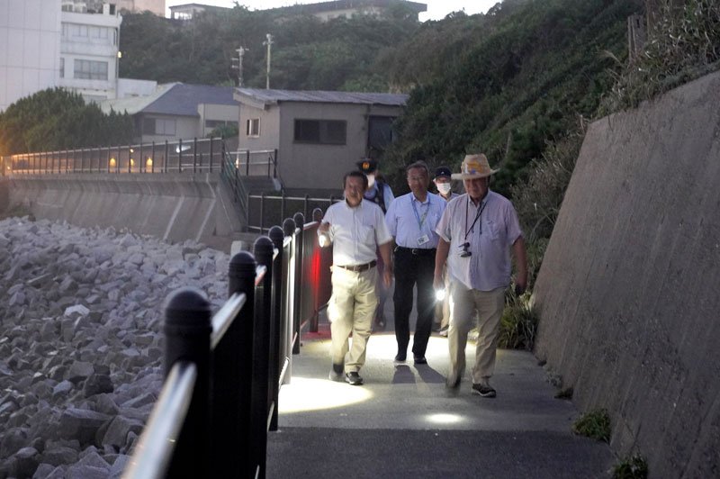 灯台下の遊歩道を明かりで照らしながら歩く合同パトロールの参加者＝銚子市