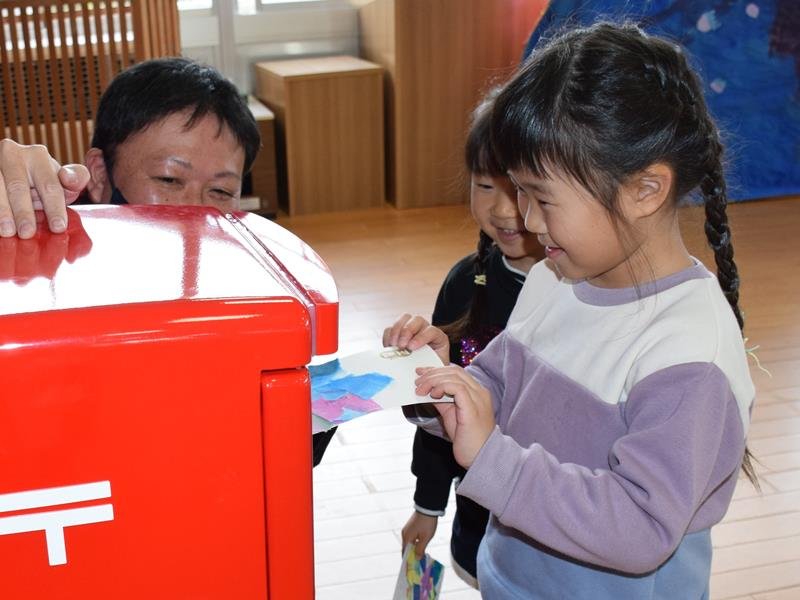 心を込めて手作りした年賀状を笑顔でポストに投かんする園児＝１９日、長生村立高根こども園
