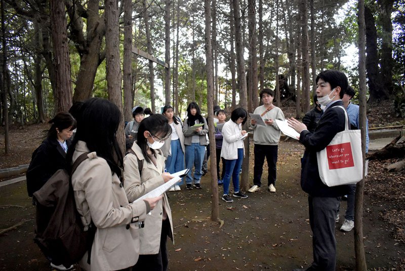 長福寺の裏山で、市教委の担当者から民話にまつわる話を聞く子ども記者ら＝船橋市
