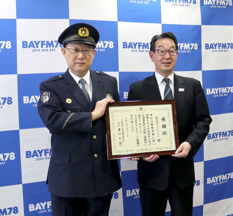 感謝状を受け取ったベイエフエムの久保社長（右）と千葉東署の広川署長＝千葉市美浜区のベイエフエム本社