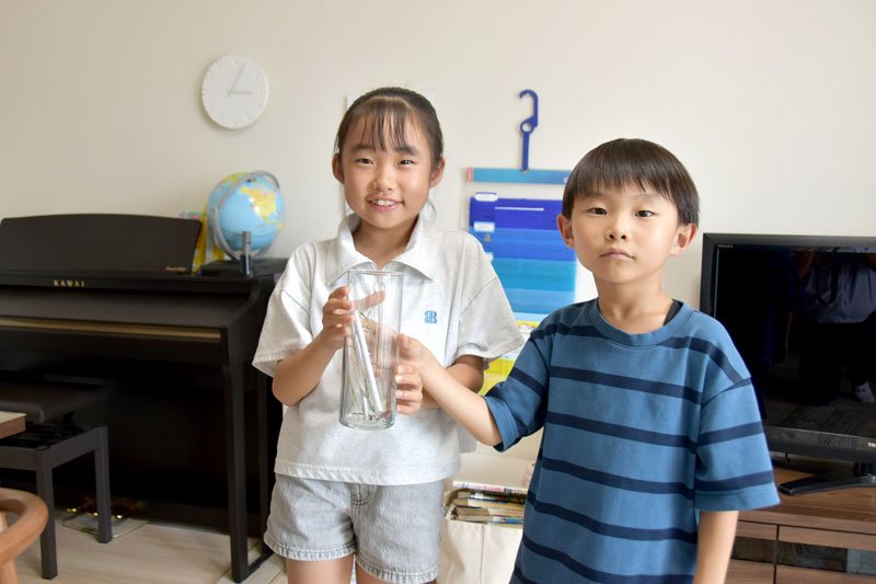 赤いバッタを入れた瓶を持つ芽唯さん（左）と悠成さん＝千葉市中央区
