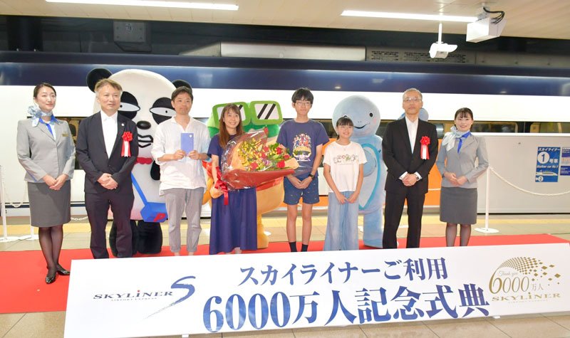 京成スカイライナーの利用６０００万人目となった家族（左から３～６人目）と京成電鉄の持永本部長（右から２人目）ら式典参加者＝３０日、成田市