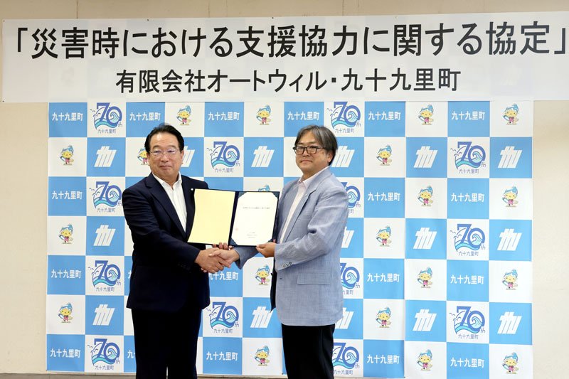 協定書を手に握手をするオートウィルの飯田社長（右）と浅岡町長