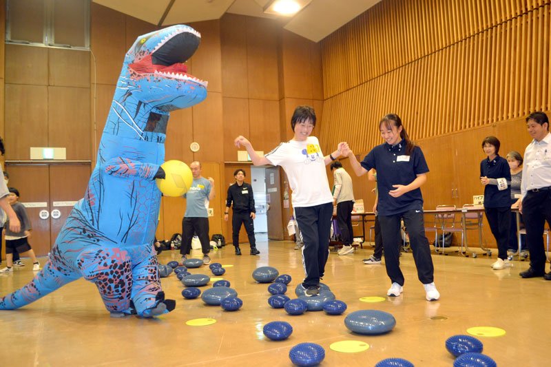 学生にサポートしてもらいながらバランスディスクの上を歩く参加者＝１８日、佐倉市立中央公民館