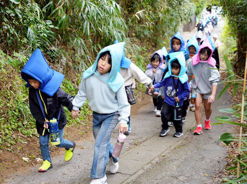 訓練で防災ずきんをかぶり手をつないで高台へ避難する双葉小児童＝５日、銚子市