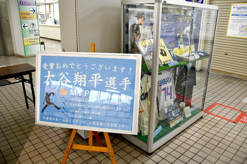 鎌ケ谷市役所１階に置かれた大谷選手の米大リーグナ・リーグＭＶＰ受賞を祝う看板。ガラスケースには日ハム入団時の手形が常設されている