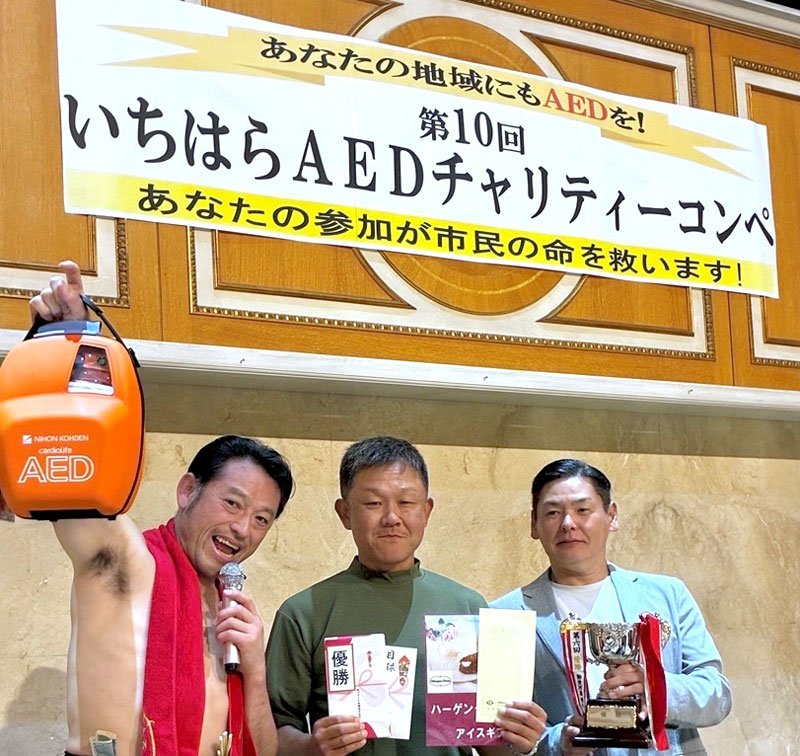 浄財で購入したＡＥＤを掲げるゲストのタレント、アントキの猪木さん（左）。写真右が宮崎会長＝市原市内のゴルフ場