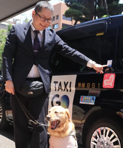 タクシーに張られたマグネットを指す松井会長と盲導犬の「ウパム」＝千葉市中央区
