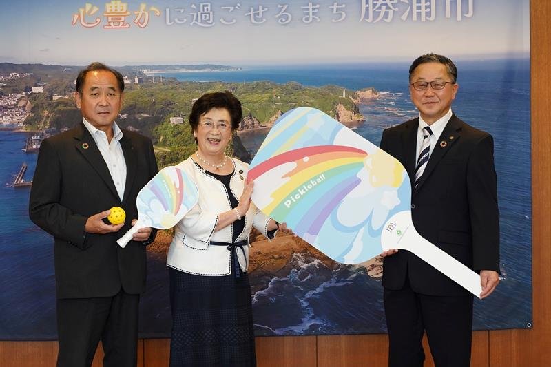 影用の大きなパドルを手にする「東急リゾートタウン勝浦」稲見統括総支配人（右）と照川市長（中央）、岩瀬好央教育長＝勝浦市役所