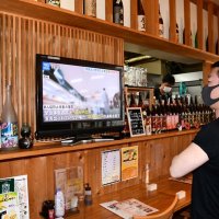 店のテレビで政府が新型コロナ特措法などの改正案を閣議決定したと発表するニュースを見る「旨いもん食堂かどや」店主の沢永さん＝２２日午前、千葉市中央区