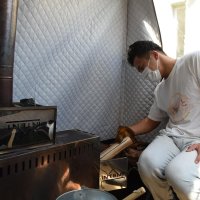 テント内でストーブにまきを入れる望月さん
