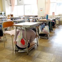 地震発生の放送とともに机の下に隠れる児童