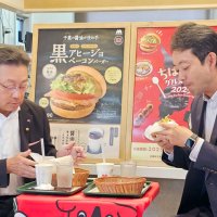県内のモスバーガーで期間限定で発売される「黒アヒージョ　ベーコンバーガー」を試食する熊谷知事（右）とモスフードサービスの中村社長＝１日午前、千葉市若葉区