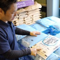 イラストが描かれていないシンプルな無洗米用のコメ袋を紹介する斎藤さん。手前は通常デザインのコメ袋＝６月、大網白里市